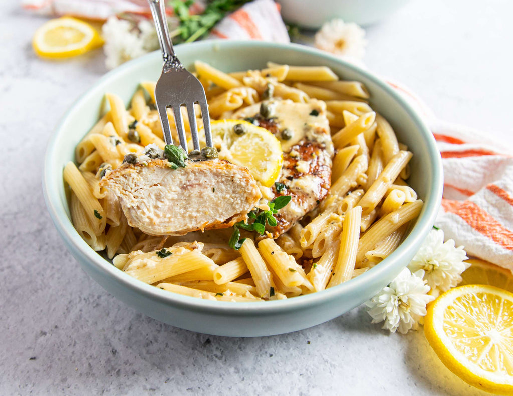 Sealand creamy lemon chicken over pasta in a bowl with fresh herbs and lemon slices