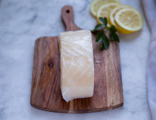 One Large, Raw Sealand Quality Foods Halibut Fillet on Wooden Cutting Board