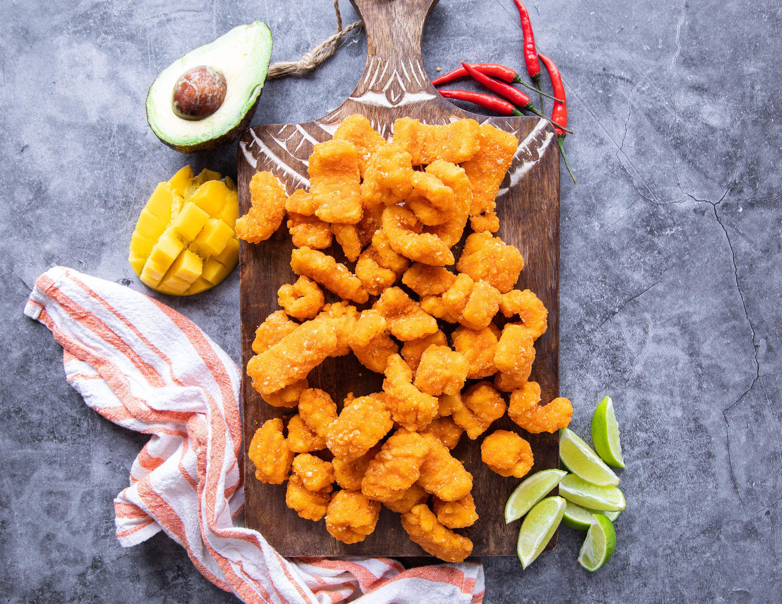 Sealand Firecracker Calamari Bites on a cutting board with fresh limes avocado chilis and mango