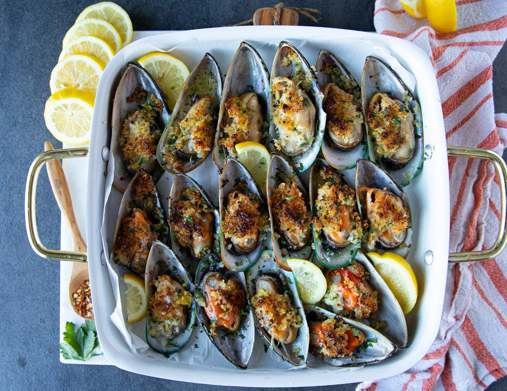 Green lipped mussels in panko breadcrumbs in a baking dish with lemons