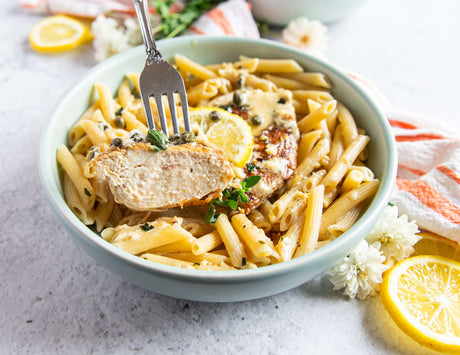 Sealand creamy lemon chicken over pasta in a bowl with fresh herbs and lemon slices