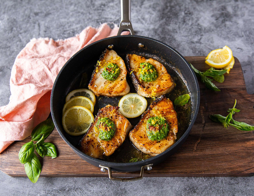 Seared Chilean sea bass with pesto and lemon slices in a skillet