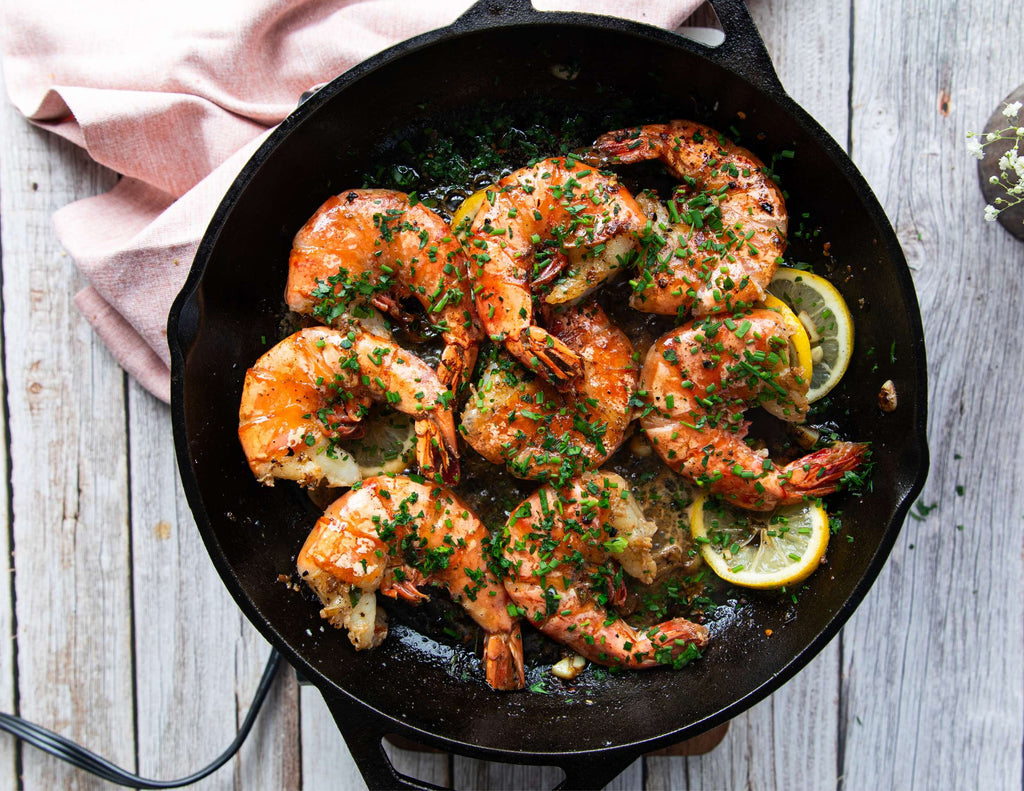 Sealand shrimp scampi in a skillet with fresh herbs and lemon slices