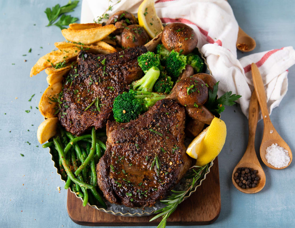 Sealand butter and rosemary veal chops on a platter with green beans, potatoes and fresh lemon