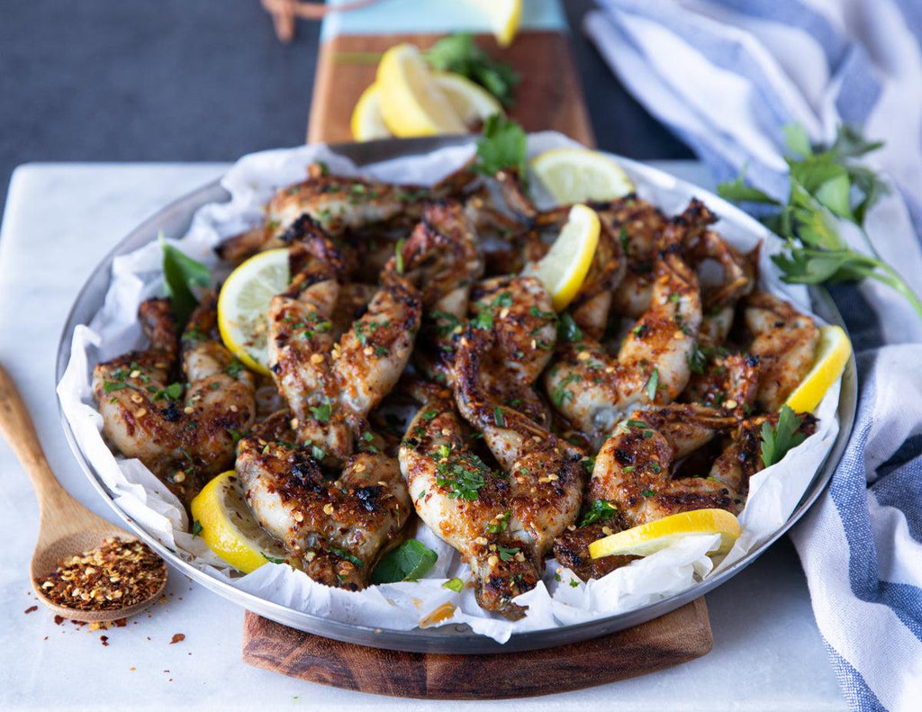 Grilled Mediterranean frog legs platter with fresh lemon slices, herbs and chili flakes