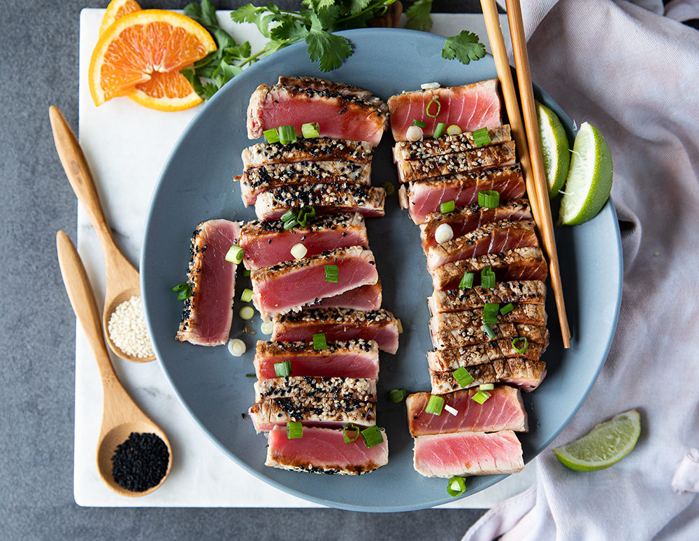 sliced and seared Sealand Quality Foods Ahi Tuna Blocks on a plate with chopsticks, lime wedges and green onions