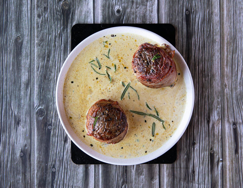 Sealand's 4oz Bacon Wrapped Tenderloin Steaks plated with rosemary in a buttery sauce.