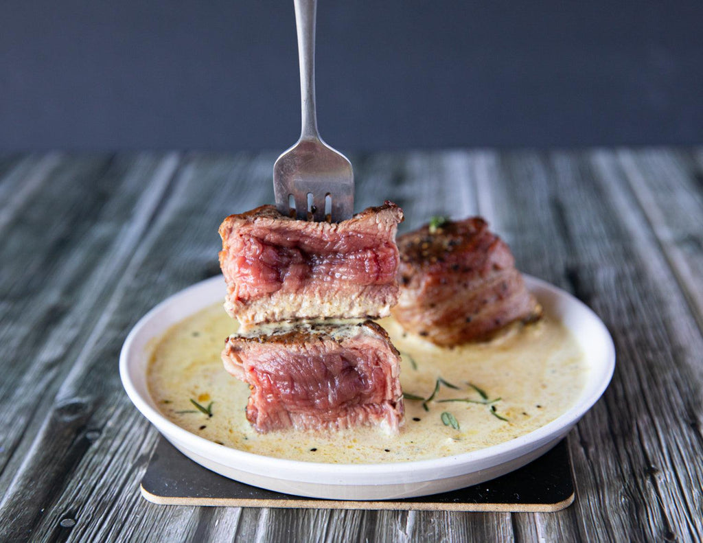 Sealand's 4oz Bacon Wrapped Tenderloin Steaks plated with rosemary in a buttery sauce.