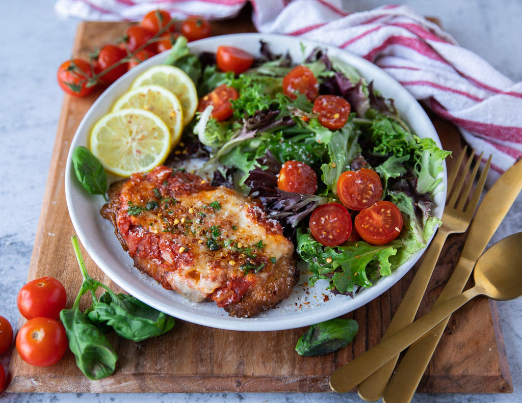 A cooked Chicken Parmigiana with a side salad and lemon slices.