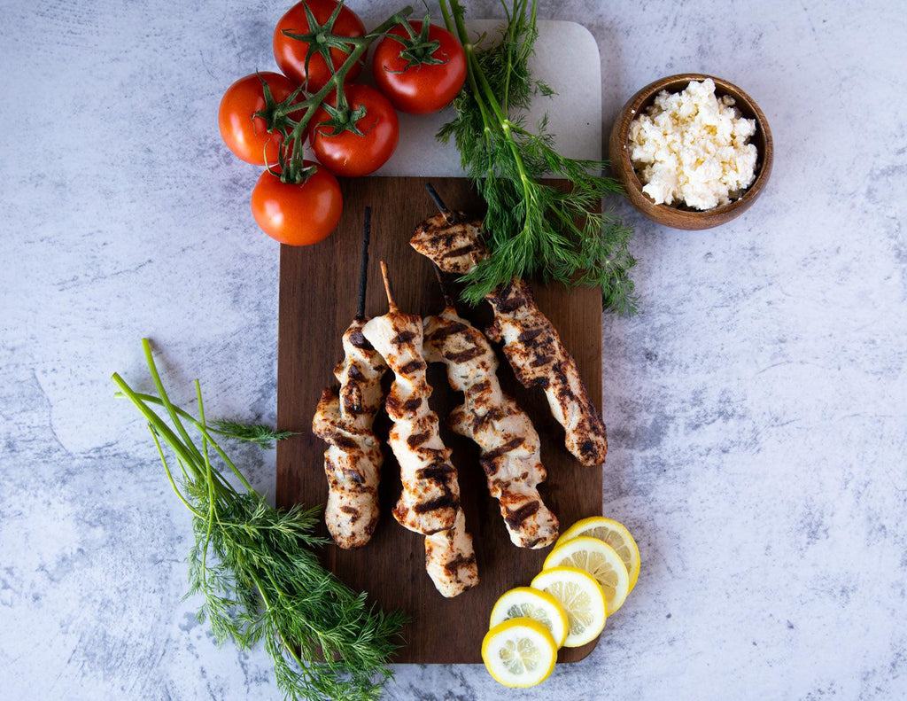 Sealand's raw Chicken Souvlaki Skewers on a cedar plank with fresh dill, tomatoes, lemon and feta cheese.