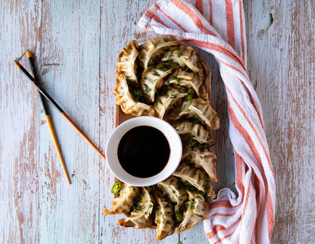 Sealand's Chicken and Vegetable Dumpling Gyozas arranged on a wooden platter with a side of soy sauce.