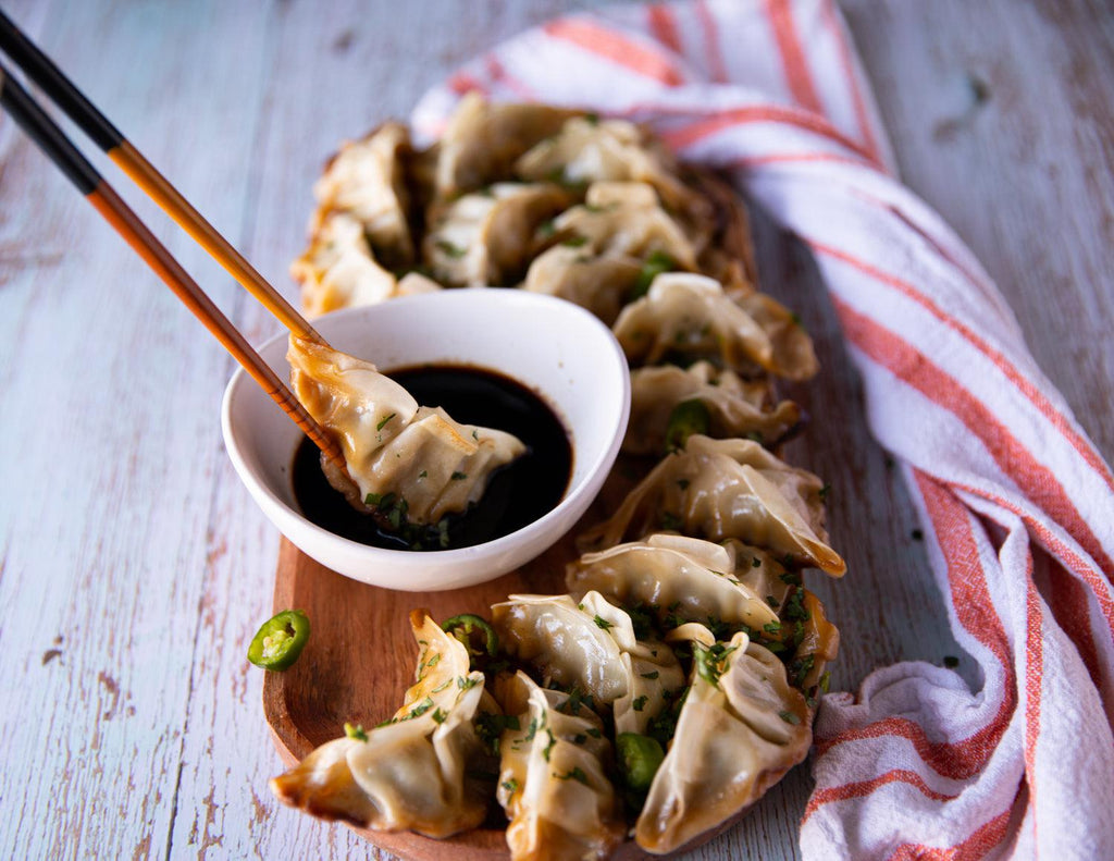 Sealand's Chicken and Vegetable Dumpling Gyozas on a wooden platter and dipped in soy sauce.