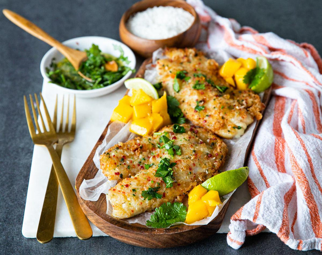 Cooked Coconut Crusted Tilapia FIllets on a wooden platter with mango and a lime wedge.