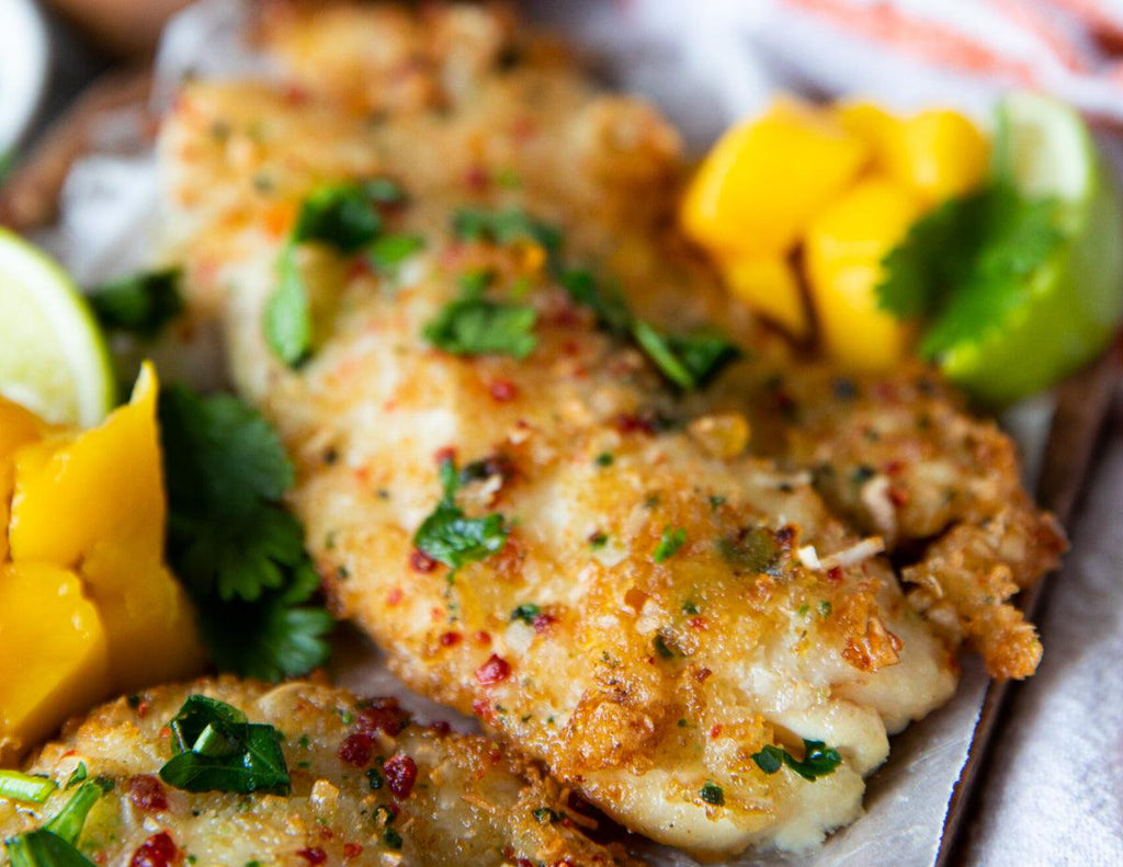 Cooked Coconut Crusted Tilapia FIllets on a wooden platter with mango and a lime wedge.