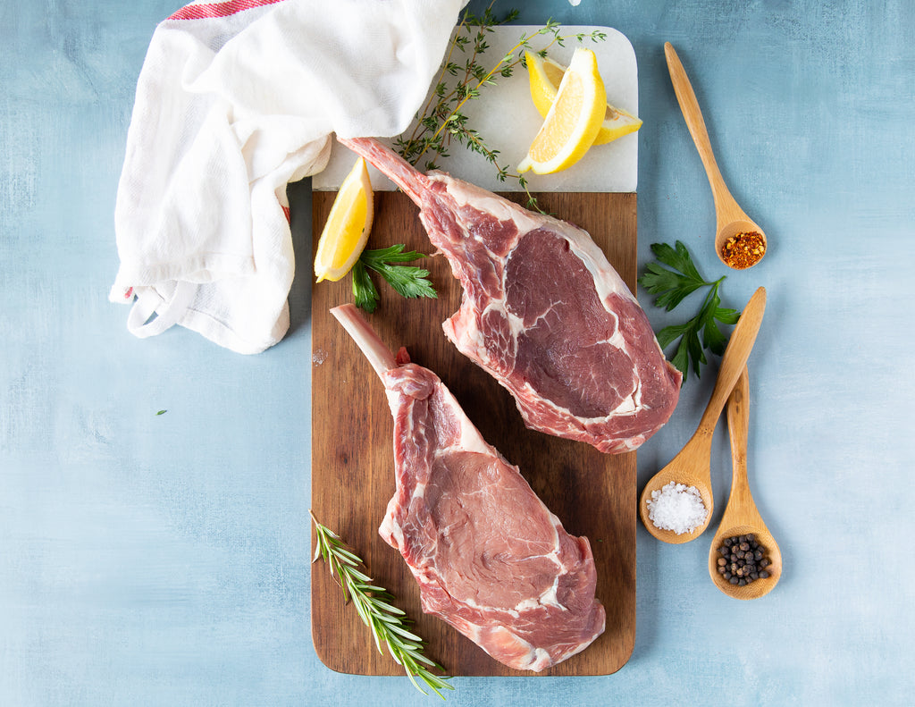 Raw French Cut Grain Fed Veal Chops with sprigs of rosemary and thyme.