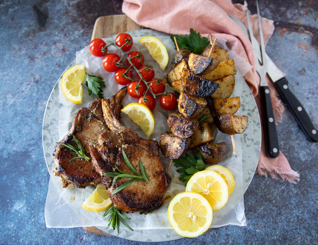 Sealand's French Cut Pork Chops on a platter with potatoes, tomatoes and fresh lemon slices.