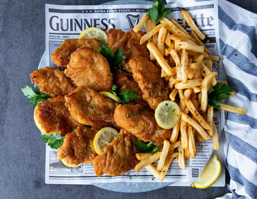Guinness Battered Cod with a side of fries and sprinkled with fresh herbs and lemon slices.