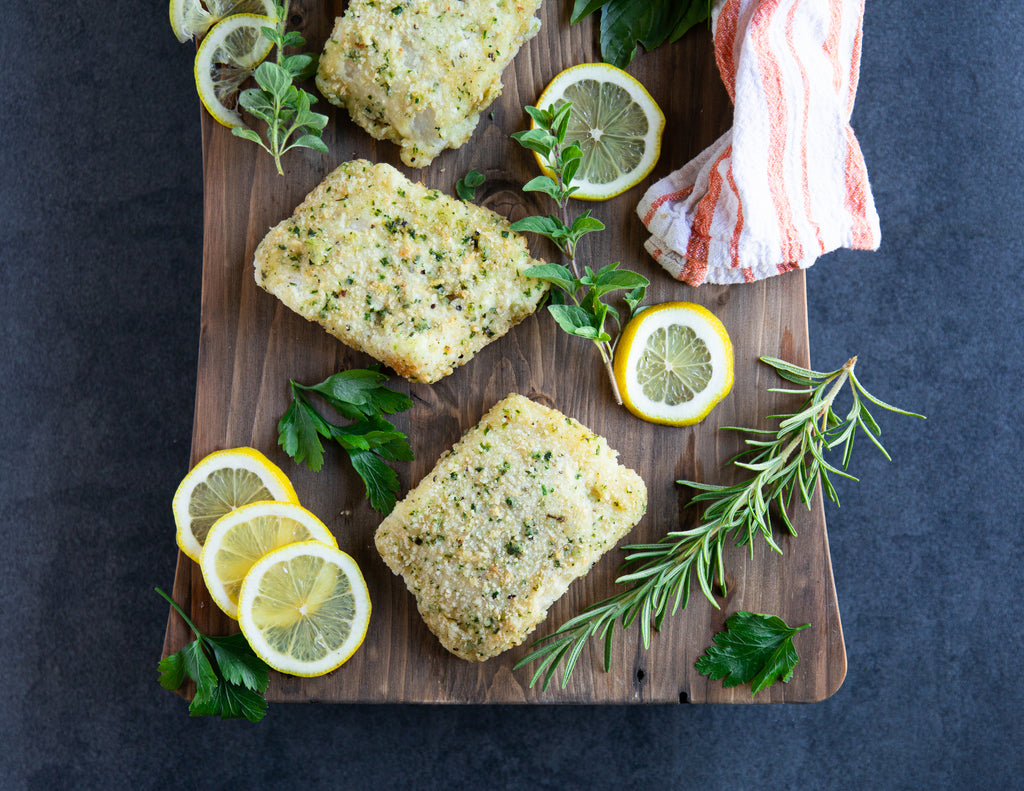 Uncooked Herb Crusted Cod Fillets on a wooden platter with fresh herbs.
