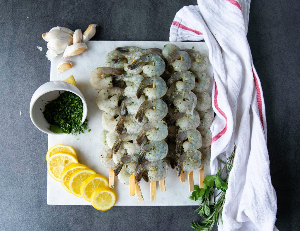 Raw Herb and Garlic Shrimp Skewers on a Cutting Board with Lemons