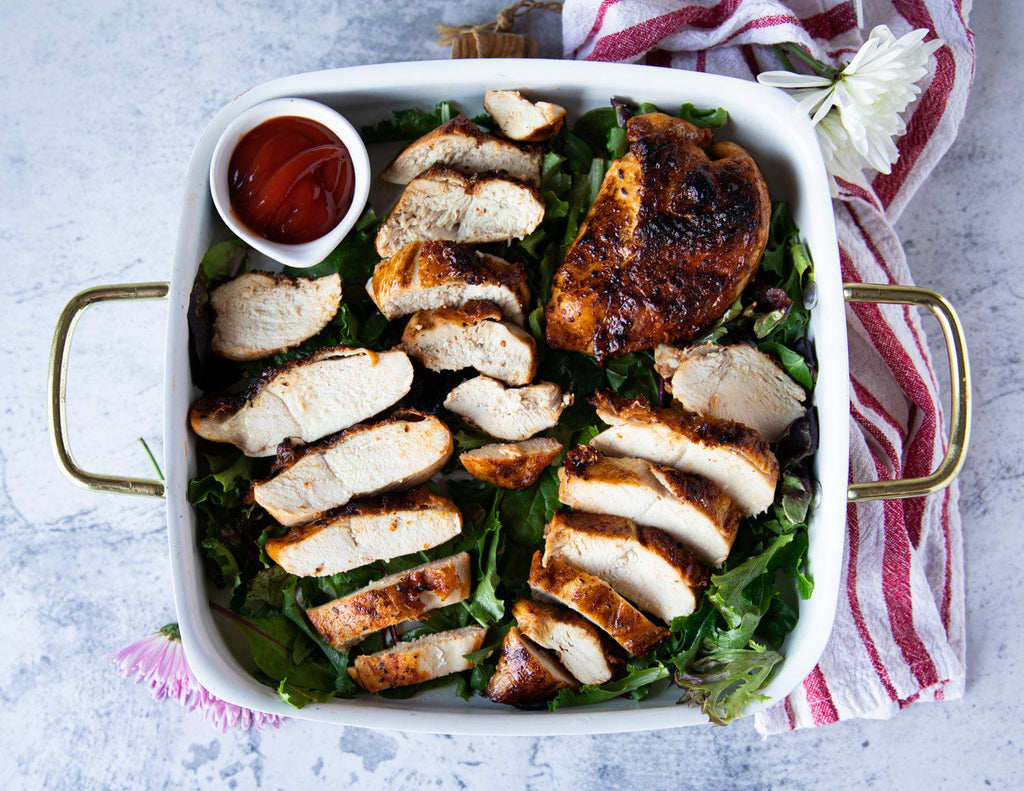Sealand's Seasoned Skin On BBQ Chicken Breasts served on a bed of greens and plated with a side of ketchup.