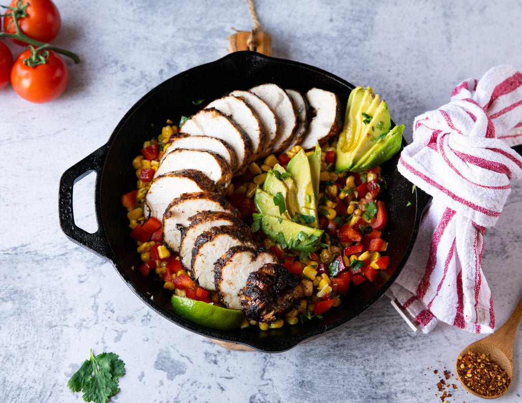 Turkey Tenderloins cooked in a cast iron skillet with a corn and tomato medley and avocado slices.