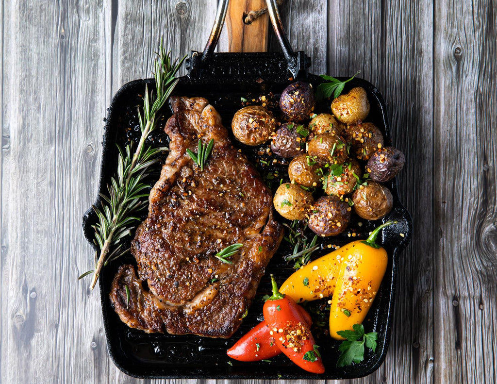 Sealand Quality Foods' whole Wagyu Ribeye Steaks seared on a cast iron skillet with peppers and potatoes.